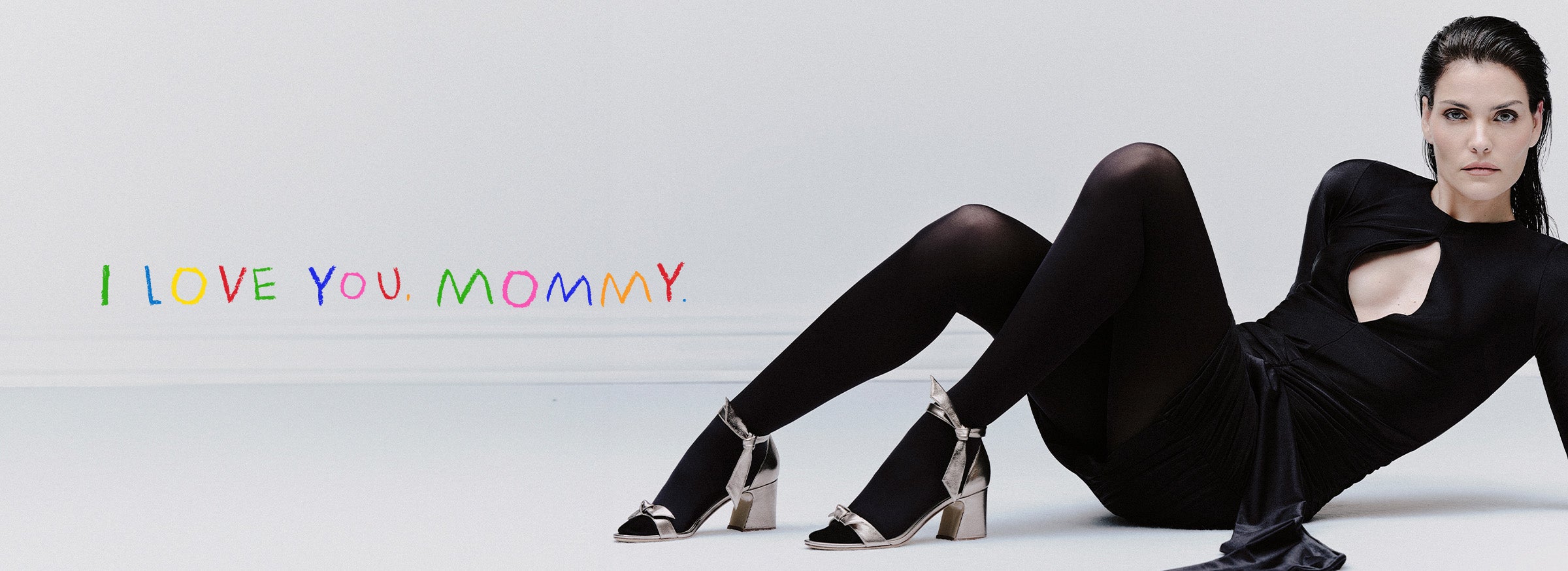 A woman elegantly lies on the ground, wearing a sleek black dress and tights. Her black hair is brushed back as she showcases the Clarita Curve 60 in Metallic Luna Shade. The touching text reads: I LOVE YOU MOMMY.