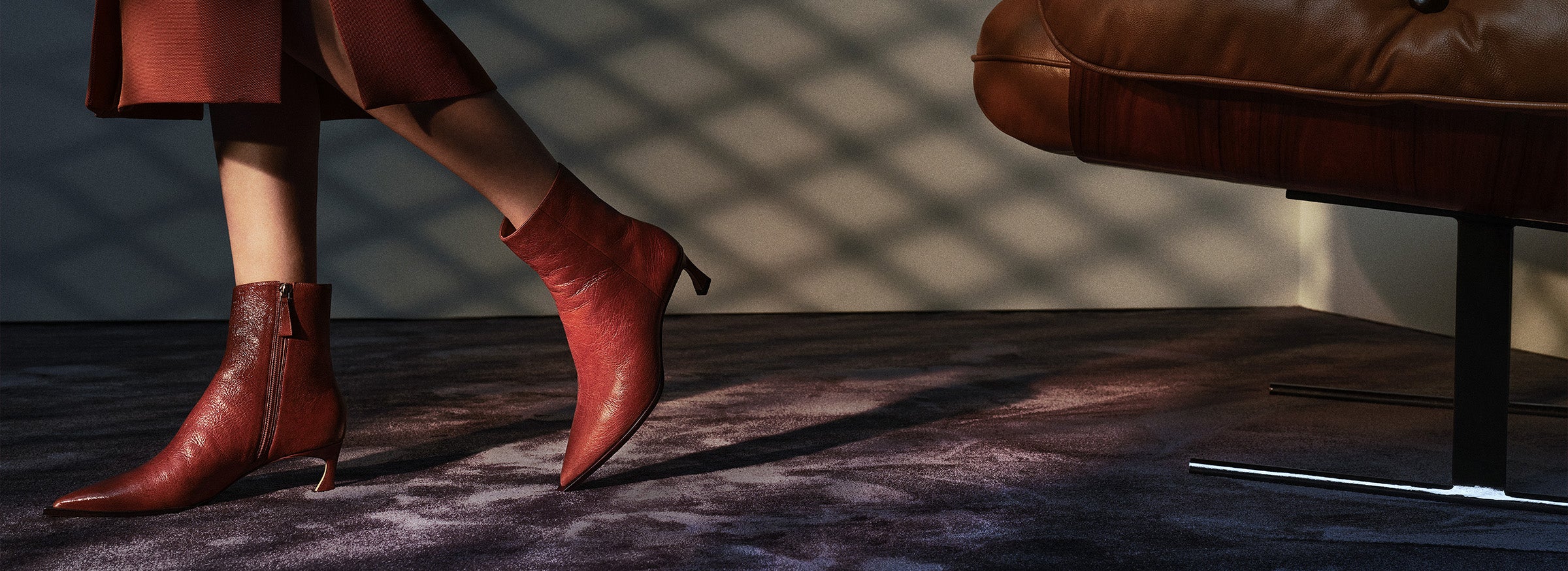 A close-up of a person's legs wearing pointed-toe ankle boots in a deep red or burgundy leather. The boots have a thin, slightly flared heel.