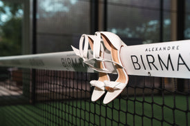 White Alexandre Birman Clarita sandals hanging from a branded padel net.