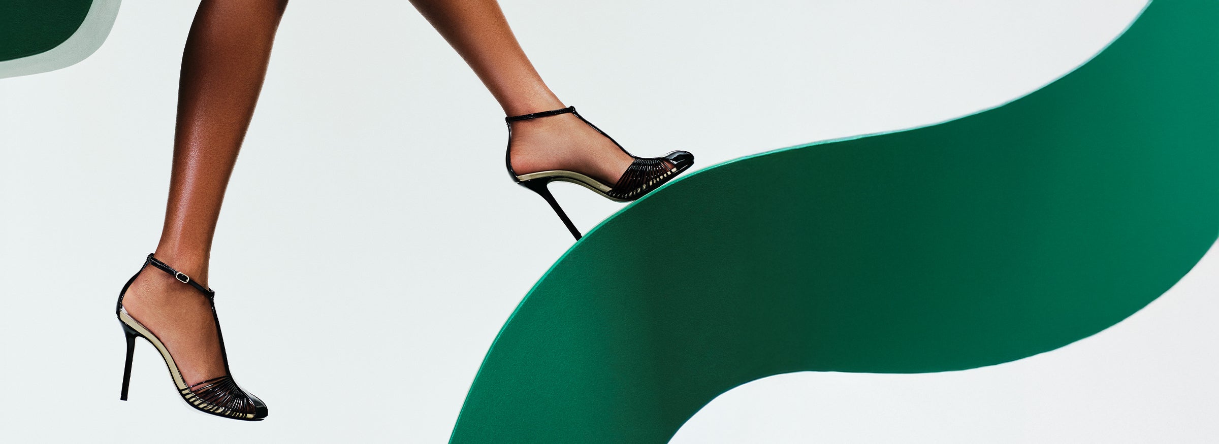  A close-up of a person in elegant black high heels stepping gracefully on a flowing green abstract shape, against a white background, conveying elegance.. Tap to shop