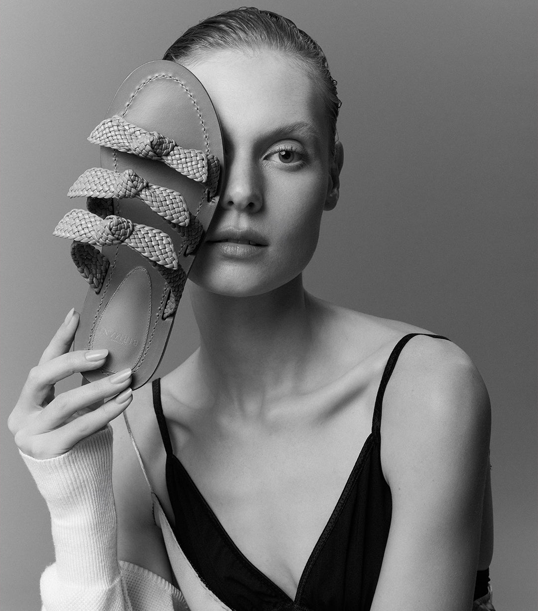 A striking black and white portrait of a woman holding the new Braided Lolita Flat, capturing the allure of timeless fashion