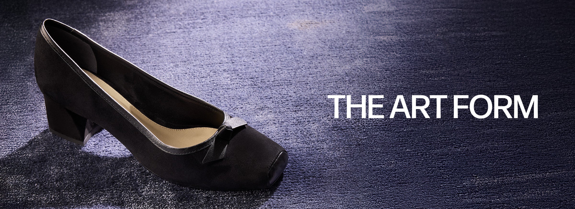  A pair of black suede pumps with square toes and a low block heel, featuring a small bow detail on the front, on a blue textured carpet. The text "THE ART FORM" is at the top.
