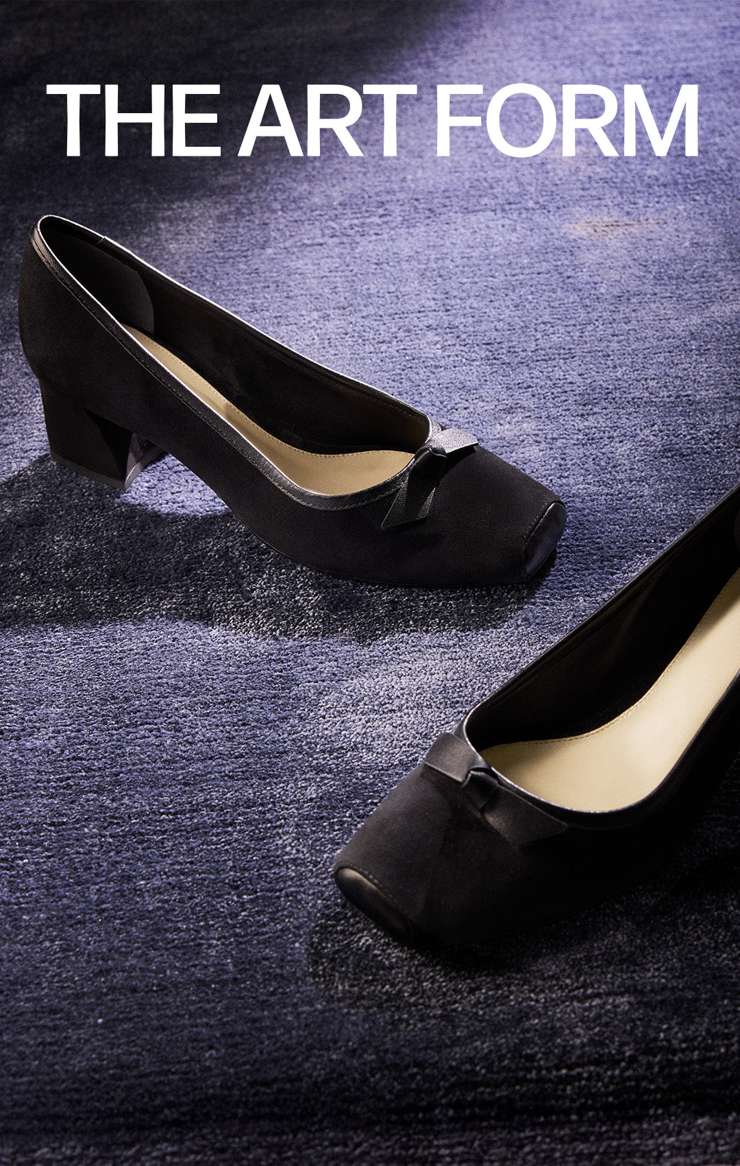  A pair of black suede pumps with square toes and a low block heel, featuring a small bow detail on the front, on a blue textured carpet. The text "THE ART FORM" is at the top.