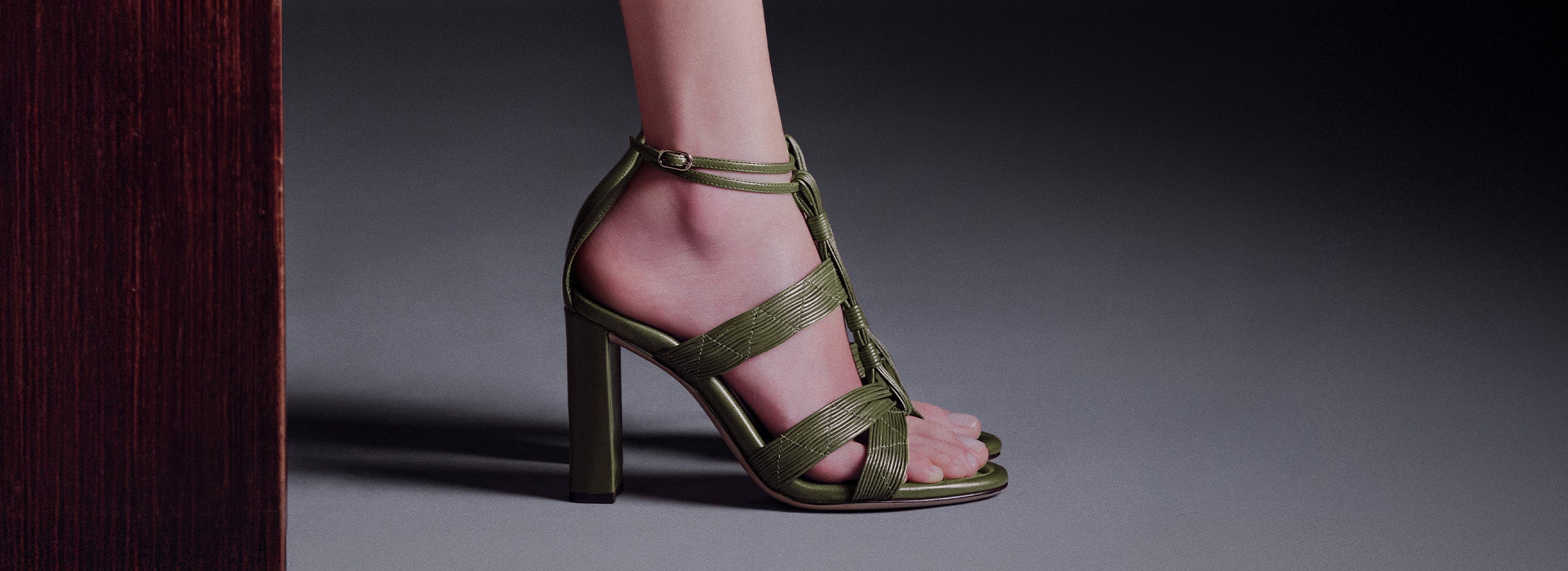  A close-up of a person's foot in a green sandal with a textured, possibly croc-embossed, finish and a block heel.