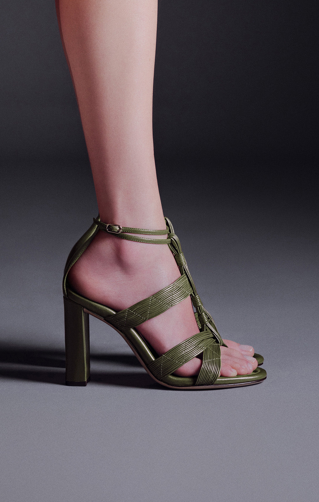  A close-up of a person's foot in a green sandal with a textured, possibly croc-embossed, finish and a block heel.
