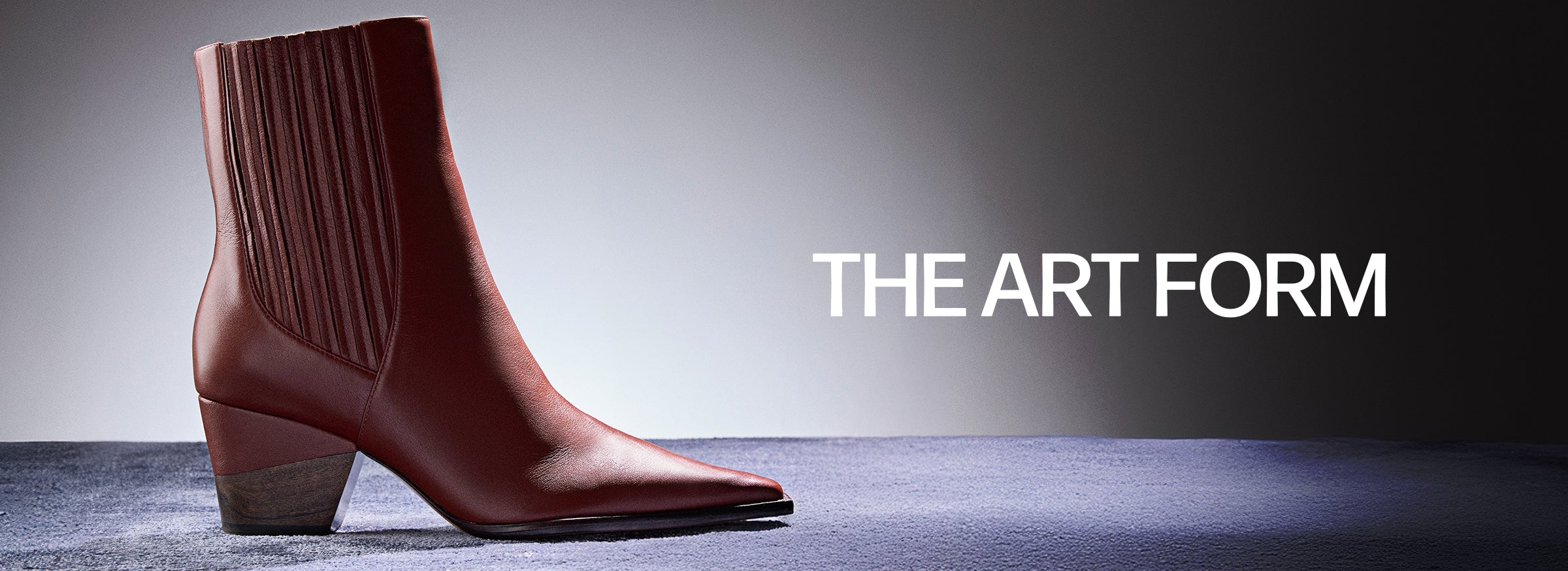  A reddish-brown leather Western-style ankle boot with a pointed toe, low stacked heel, and ribbed shaft detail. The text "THE ART FORM" is to the right of the boot.