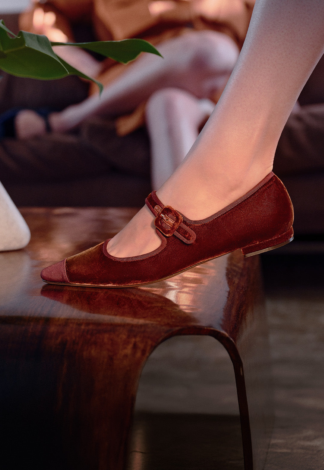  Model wearing brown trench dress and cuoio velvet ballet flats reclining on a sofa. The text "VELVET TOUCH" and the call to action "SHOP NOW" is to the bottom left of the image.