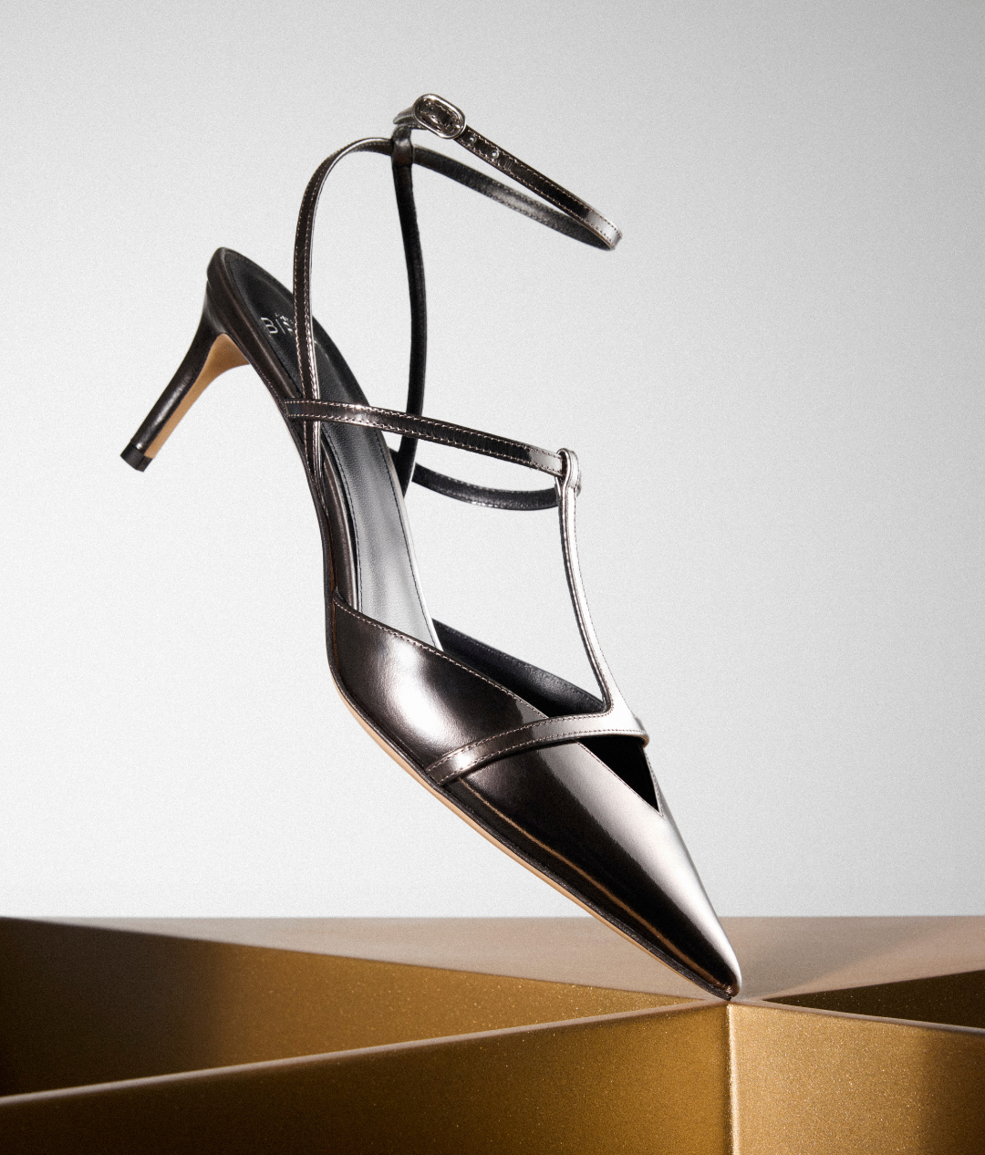 Black crystal-embellished slingback sandal displayed against a sculptural gold surface and white background. Tap to shop