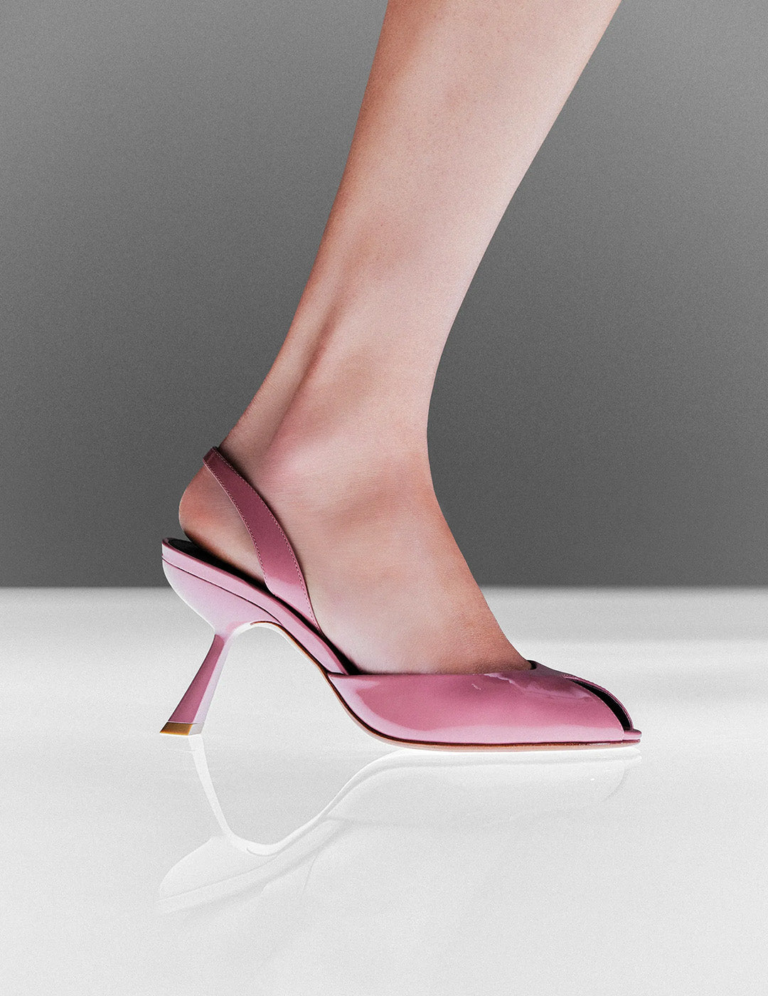 Close-up of a foot wearing an elegant pink slingback high heel on a sleek, white reflective surface. The scene conveys sophistication and style. Tap to shop.