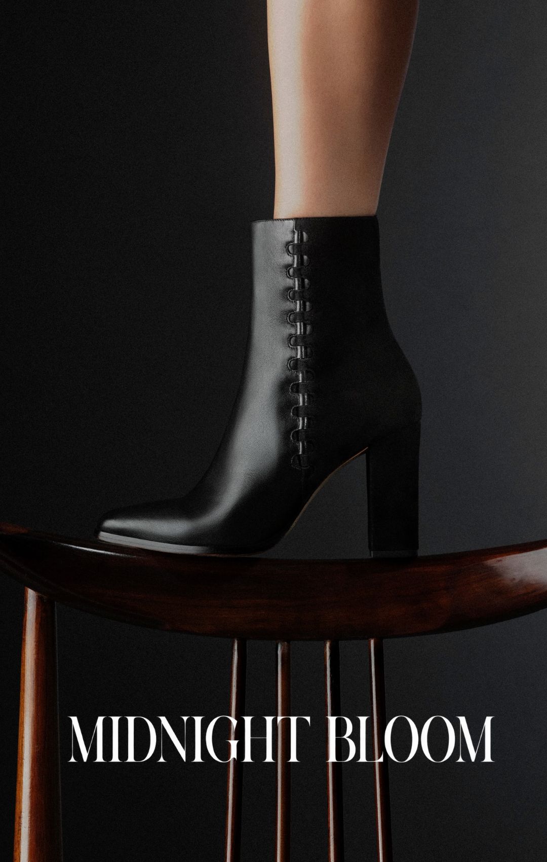  Close-up of a model in sheer black tights and glossy black Mary Jane heels with ankle straps, standing on a reflective surface beside sculptural vases. Tap to shop