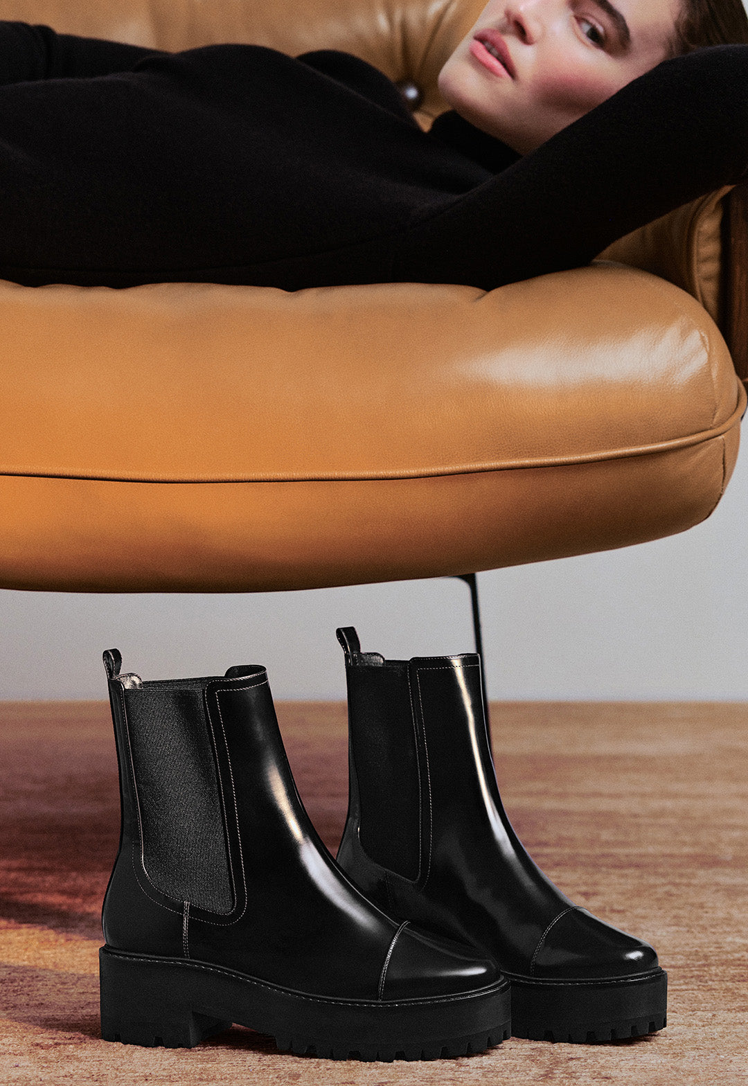  Close-up of a person's leg and foot wearing a brown suede loafer with a small bow, crouching on a bright blue carpet.