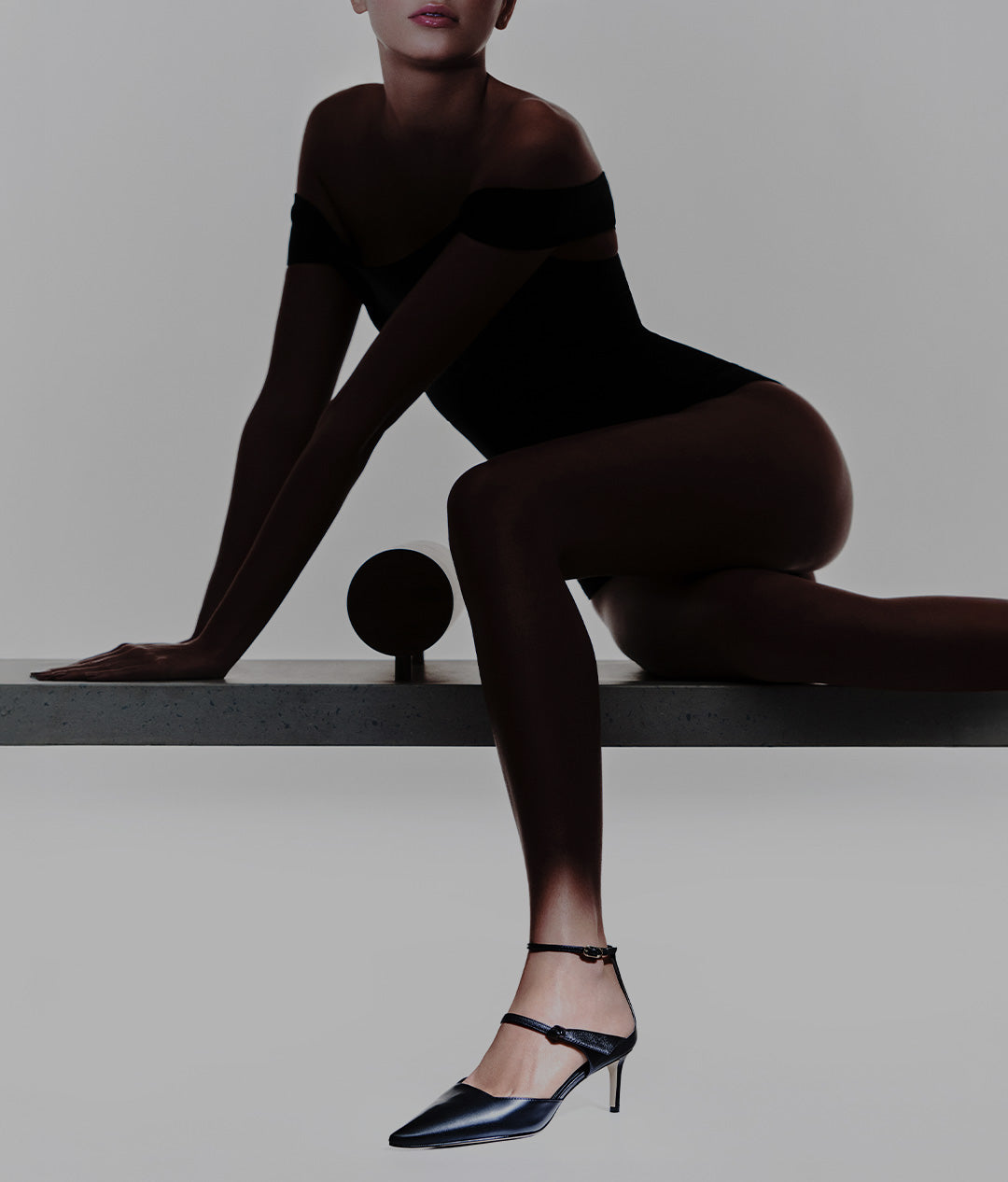  A person dressed in a black bodysuit poses on a concrete surface, wearing sleek black pointed-toe pumps with ankle straps. White text over the image reads “STRUCTURE AND MOVEMENT” and “NEW ARRIVALS.”