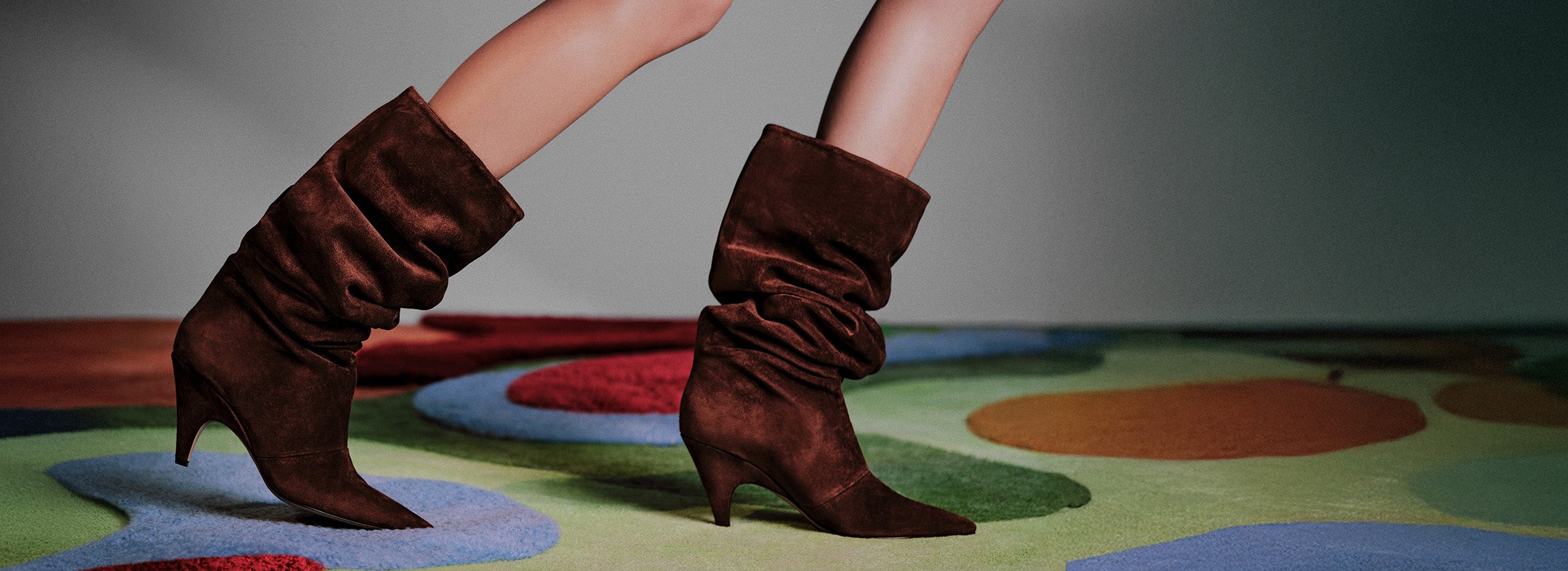  Close-up of a person's leg and foot wearing a brown suede slouch boot.