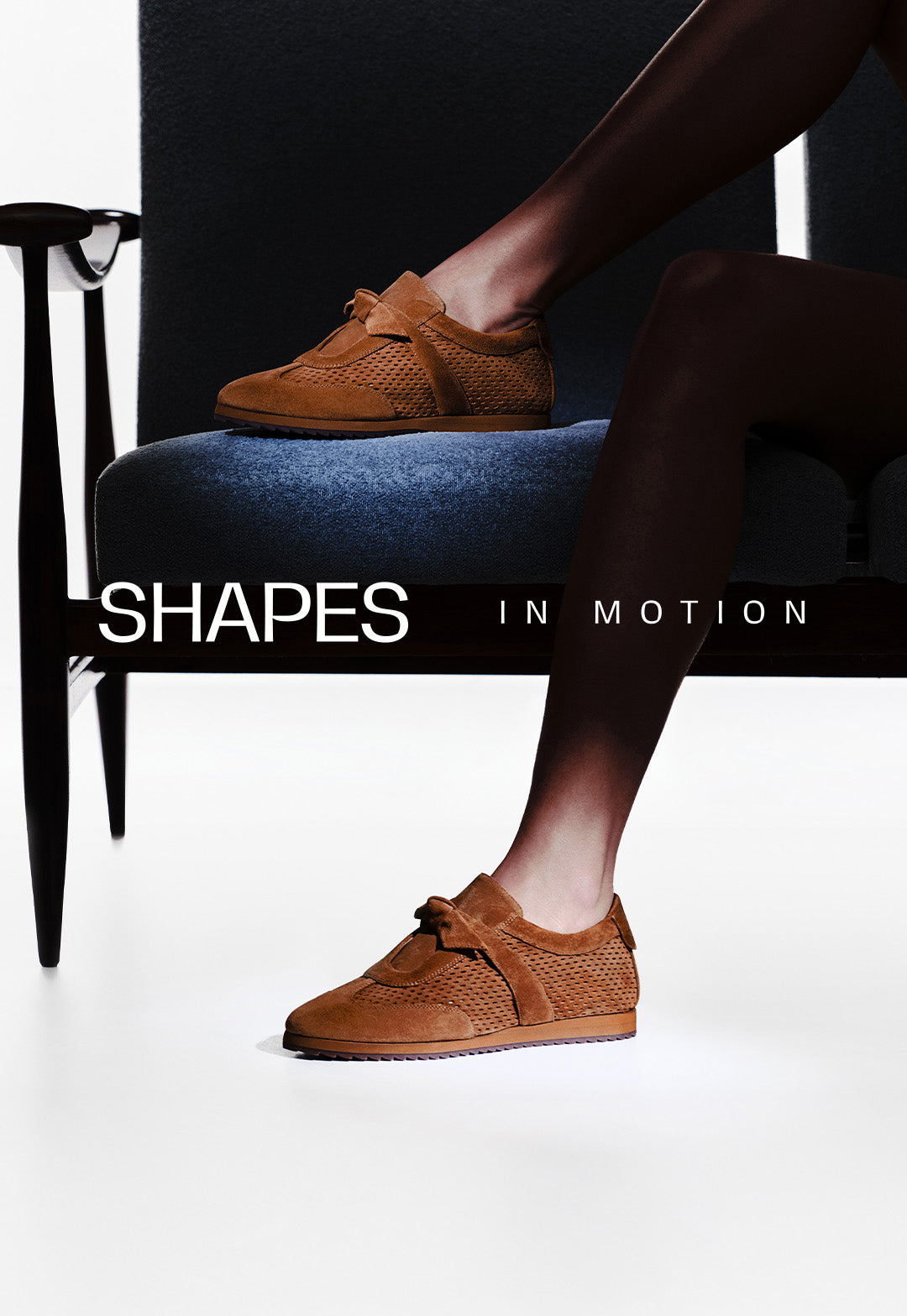  A woman sitting on a dark chair wearing brown suede perforated sneakers. Text overlay: SHAPES IN MOTION.