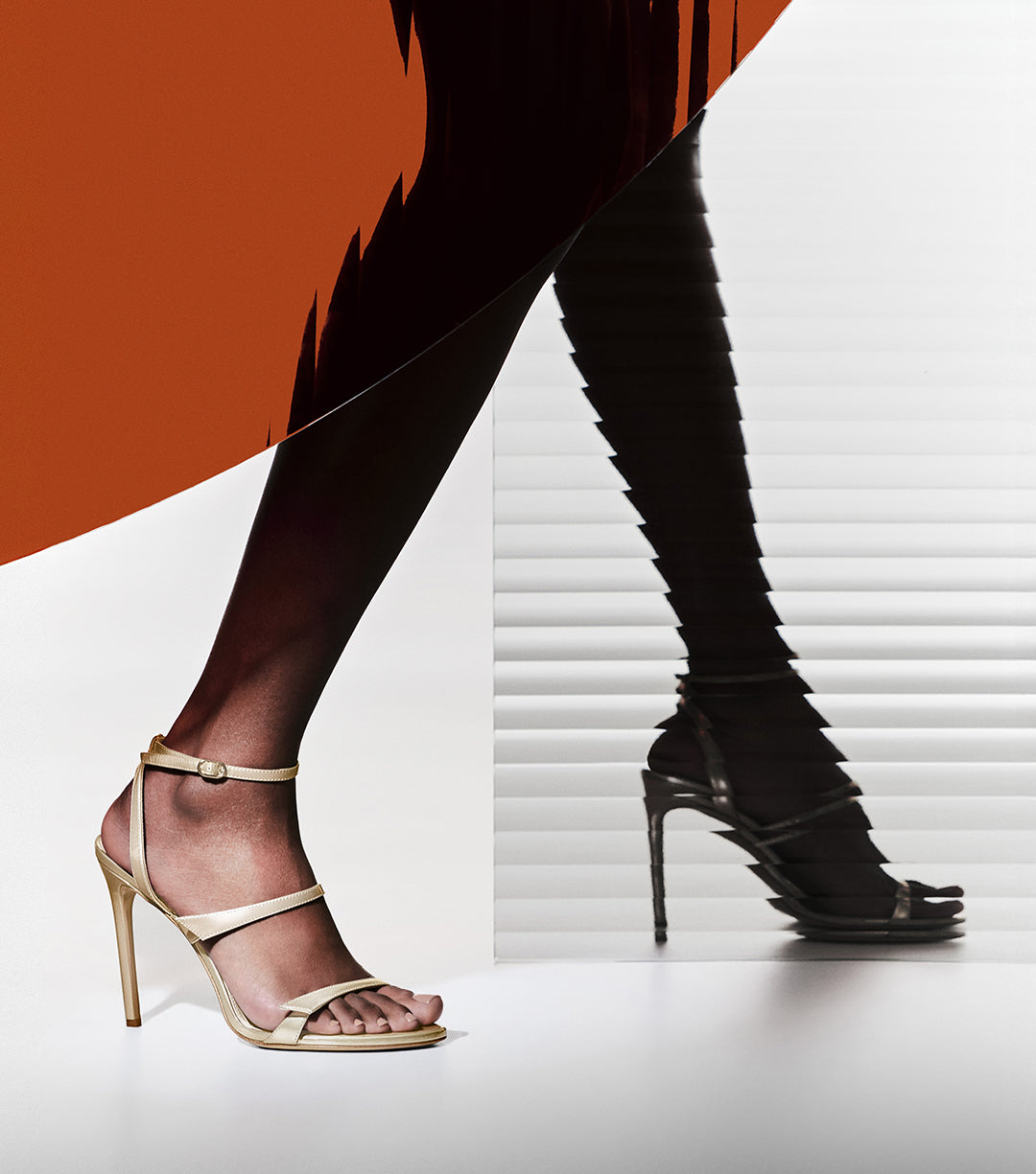 A close-up of a model's legs wearing gold strappy high-heel sandals. The composition is split, showing the lit leg on the left and a dark, distorted silhouette effect against blinds on the right.