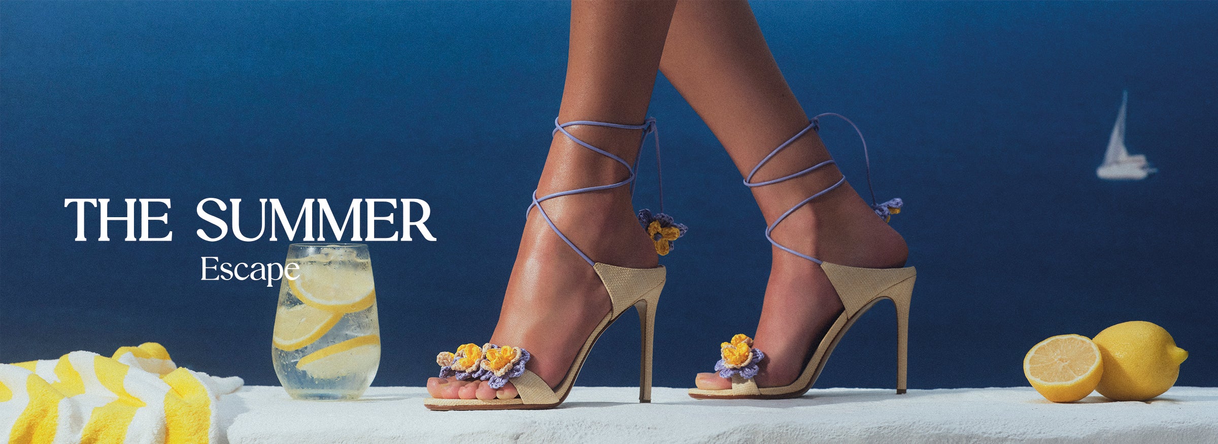  A woman in stylish high heels with floral accents stands against a blue ocean backdrop. Text reads "The Summer Escape." A cocktail and towel are nearby. Tap to shop