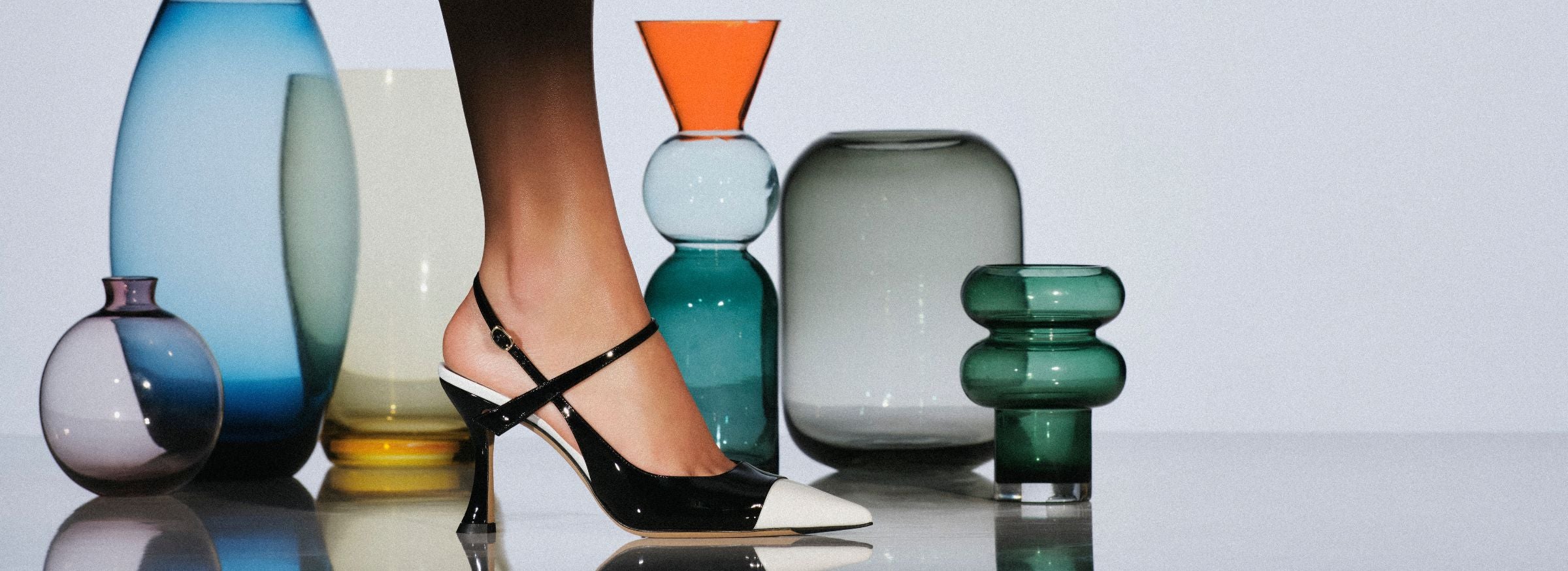  Black-and-white scissors stand open on a glossy surface, framed by amber glass vessels against a pale, minimalist background.Shop Now.