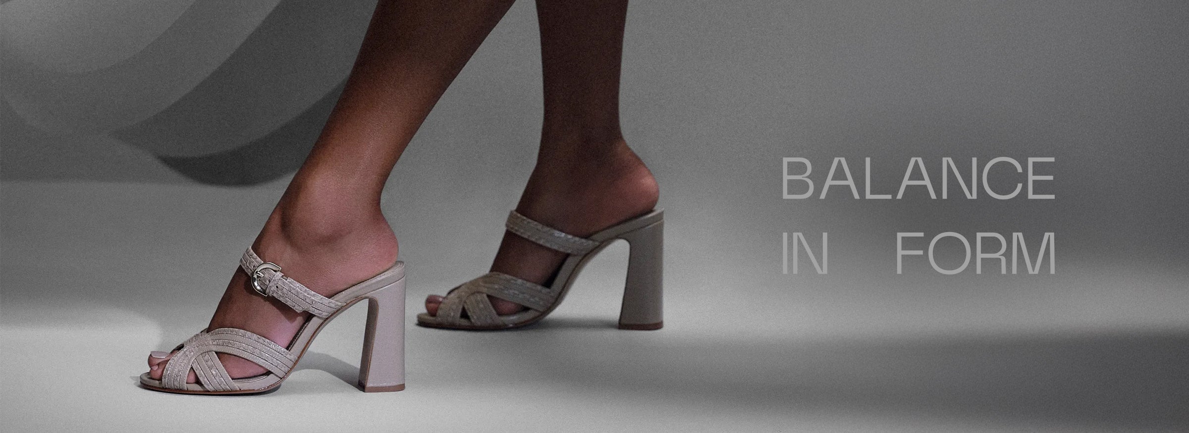  Elegant legs in beige high-heeled sandals against a minimalist gray backdrop with the text "Balance in Form" at the top, conveying sophistication. Tap to shop