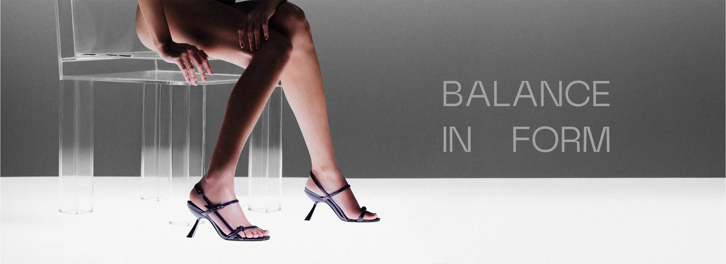  Elegant leg in a high-heeled sandal poised gracefully, with text "Balance in Form." The background features a soft grey hue, evoking sophistication. Tap to shop