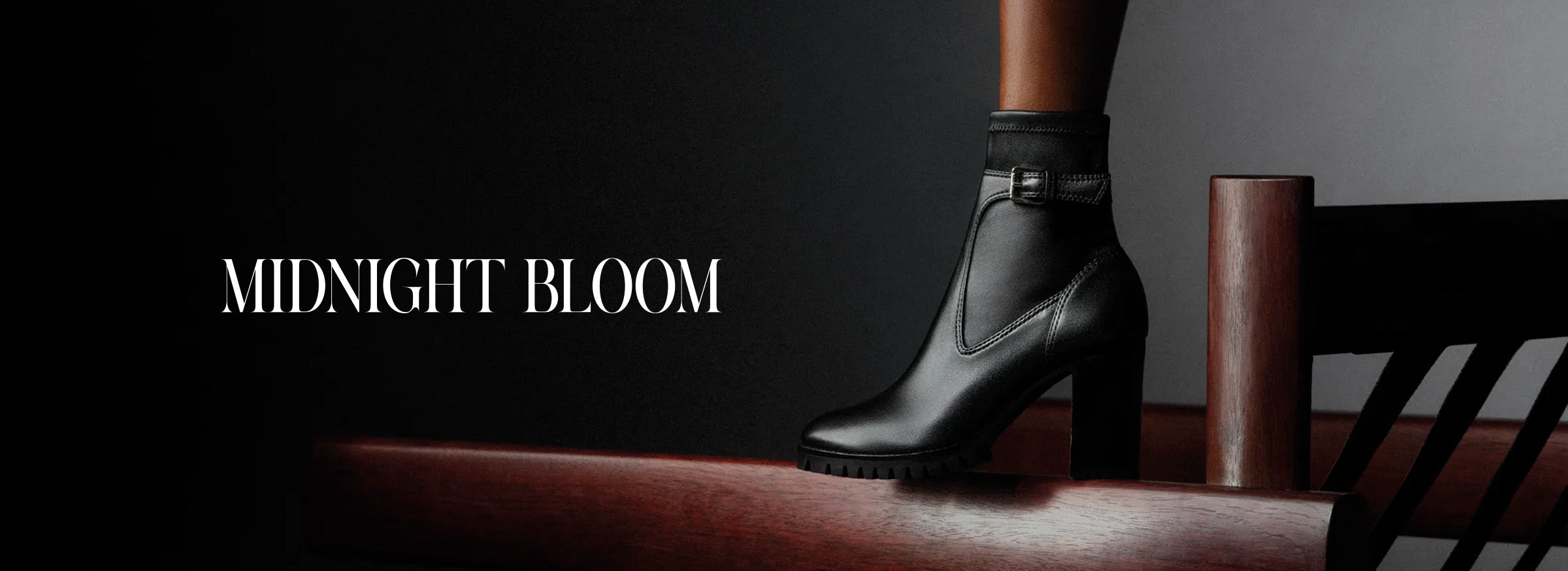  Black leather ankle boot with a high block heel rests on a wooden rail against a dark background; “MIDNIGHT BLOOM” text below, in a moody fashion ad. Shop Now.