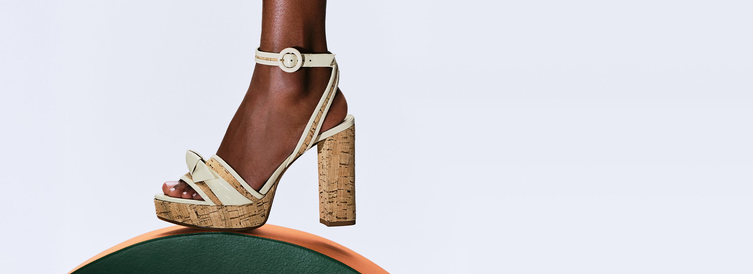  Beige cork platform sandal with ankle strap and block heel worn on a foot, standing on a green and orange curved surface. Tap to shop.
