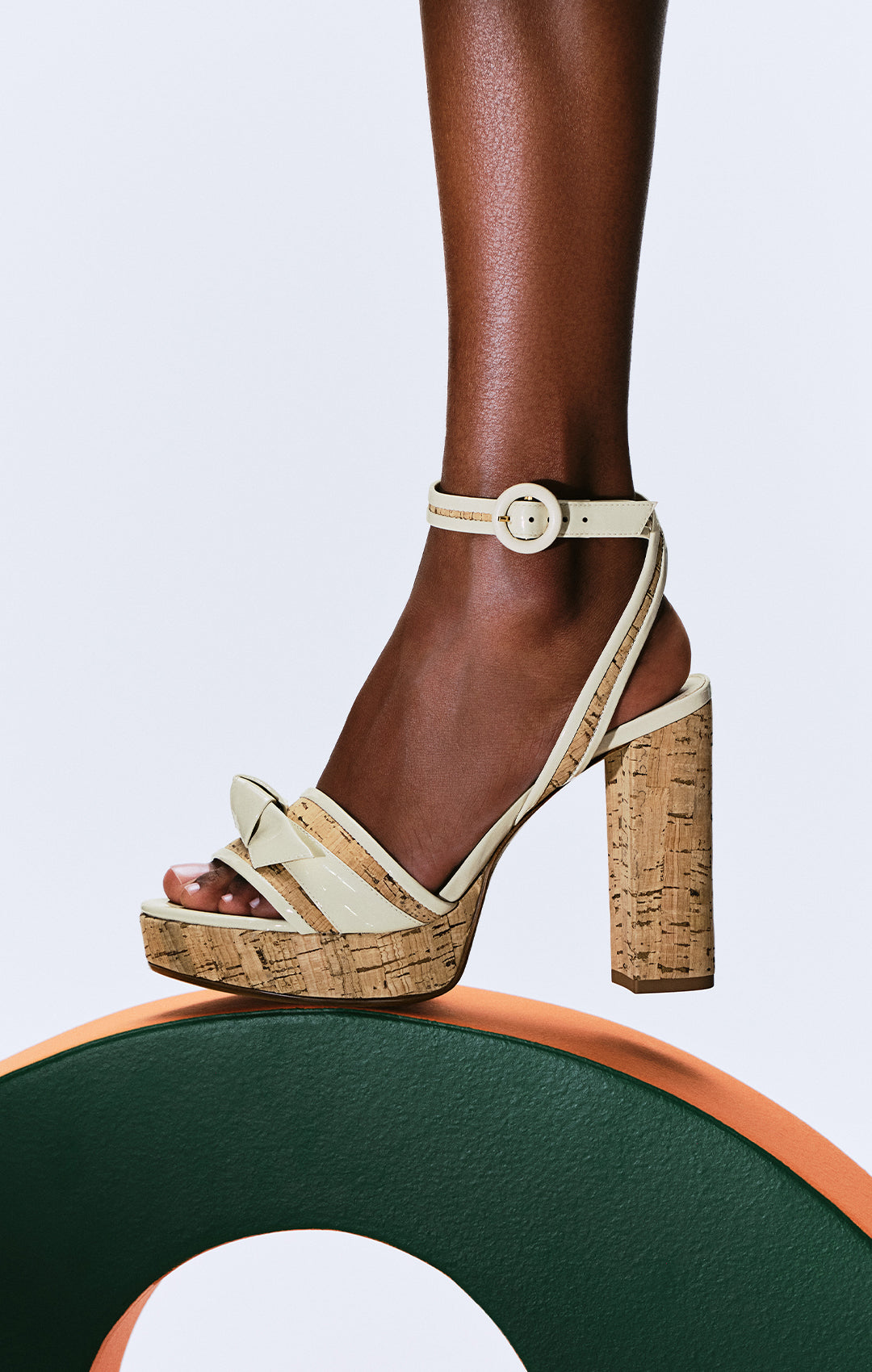  Beige cork platform sandal with ankle strap and block heel worn on a foot, standing on a green and orange curved surface. Tap to shop.